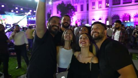 A group of men and women taking a selfie outdoors, they are surrounded by people