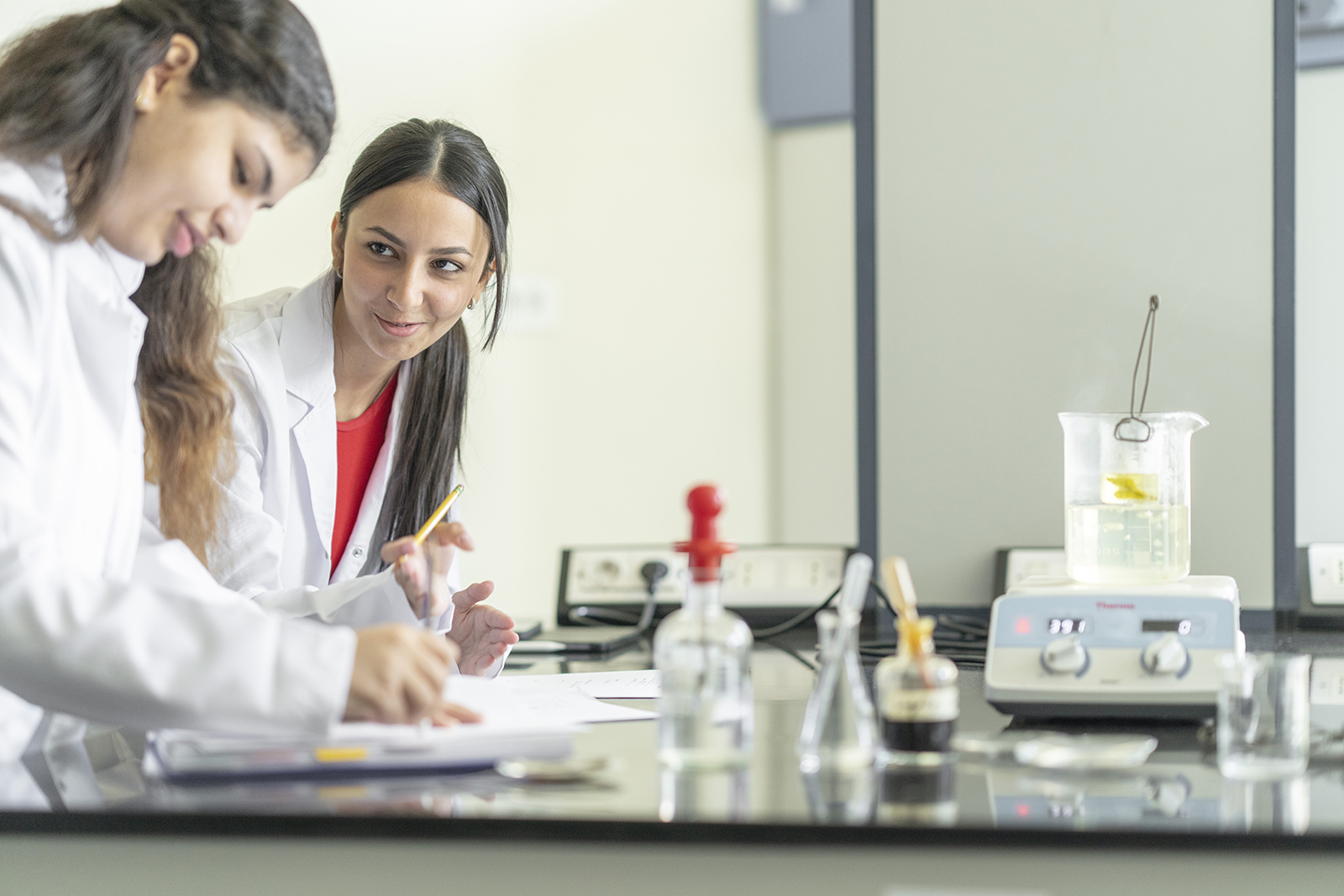 Two girls in a lab writing a report with chemical on the table in front of them