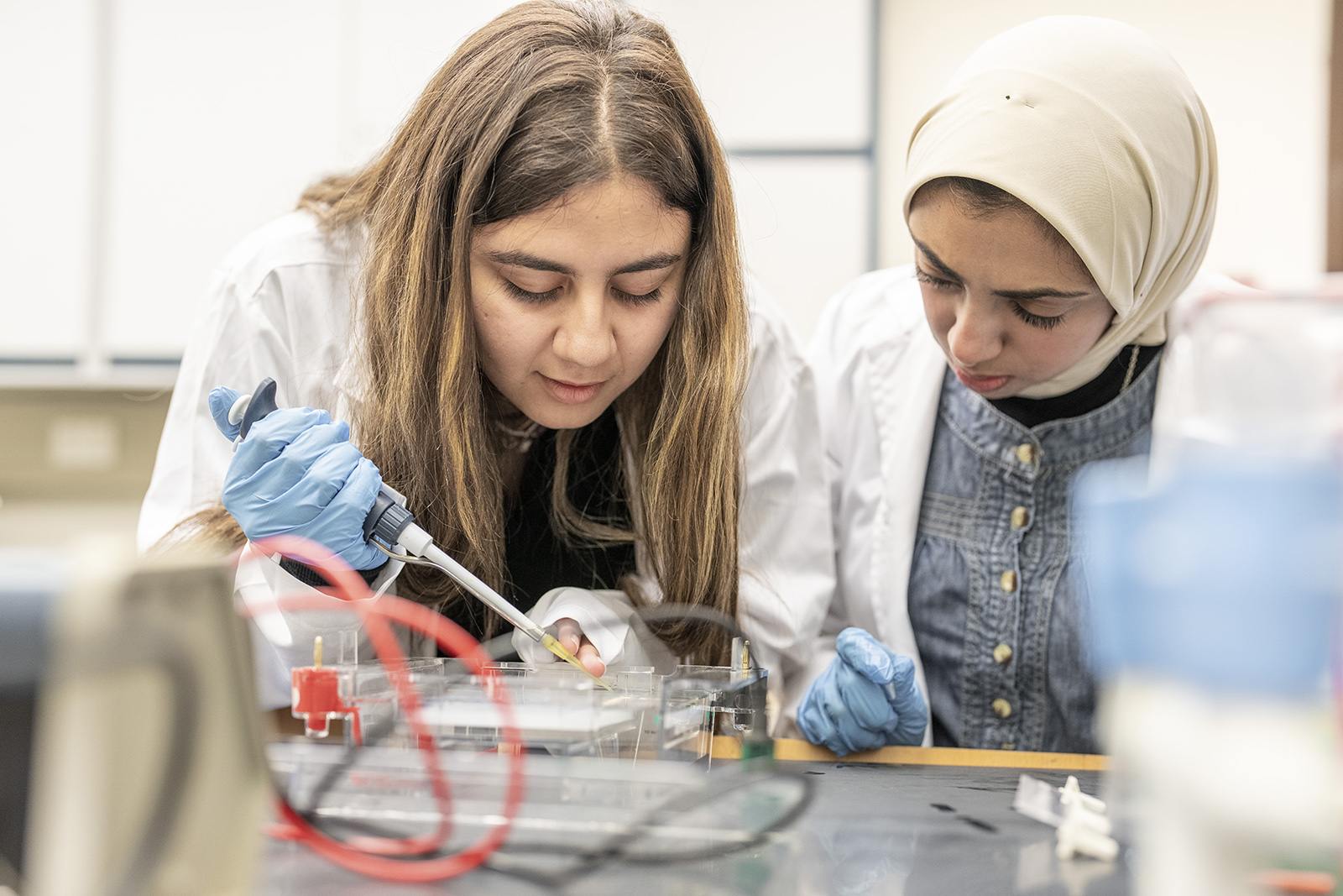 Two female students wearing a lab coat running a test in a lab