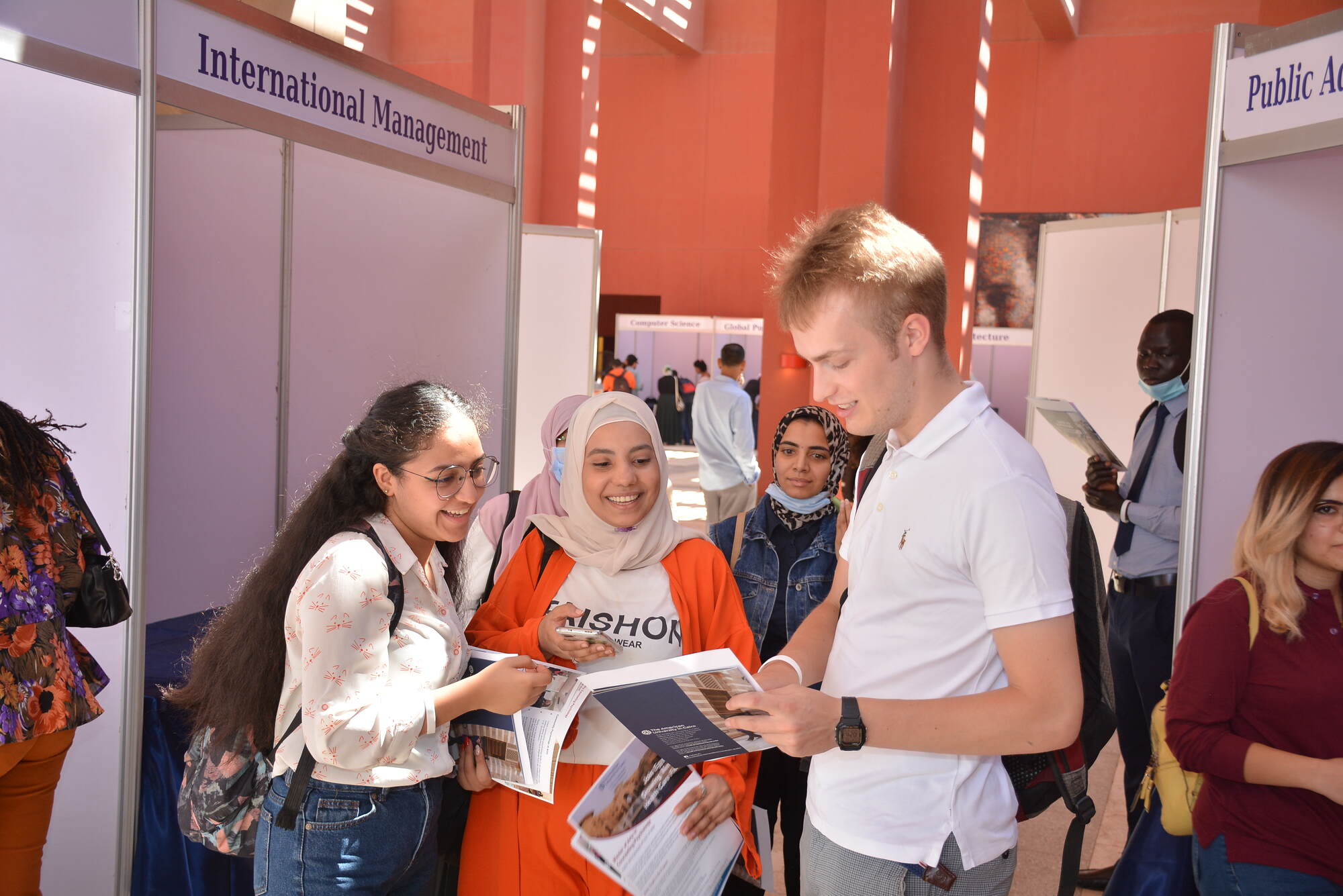 A male student showing brochure to 2 female students at Graduate Studies Open House