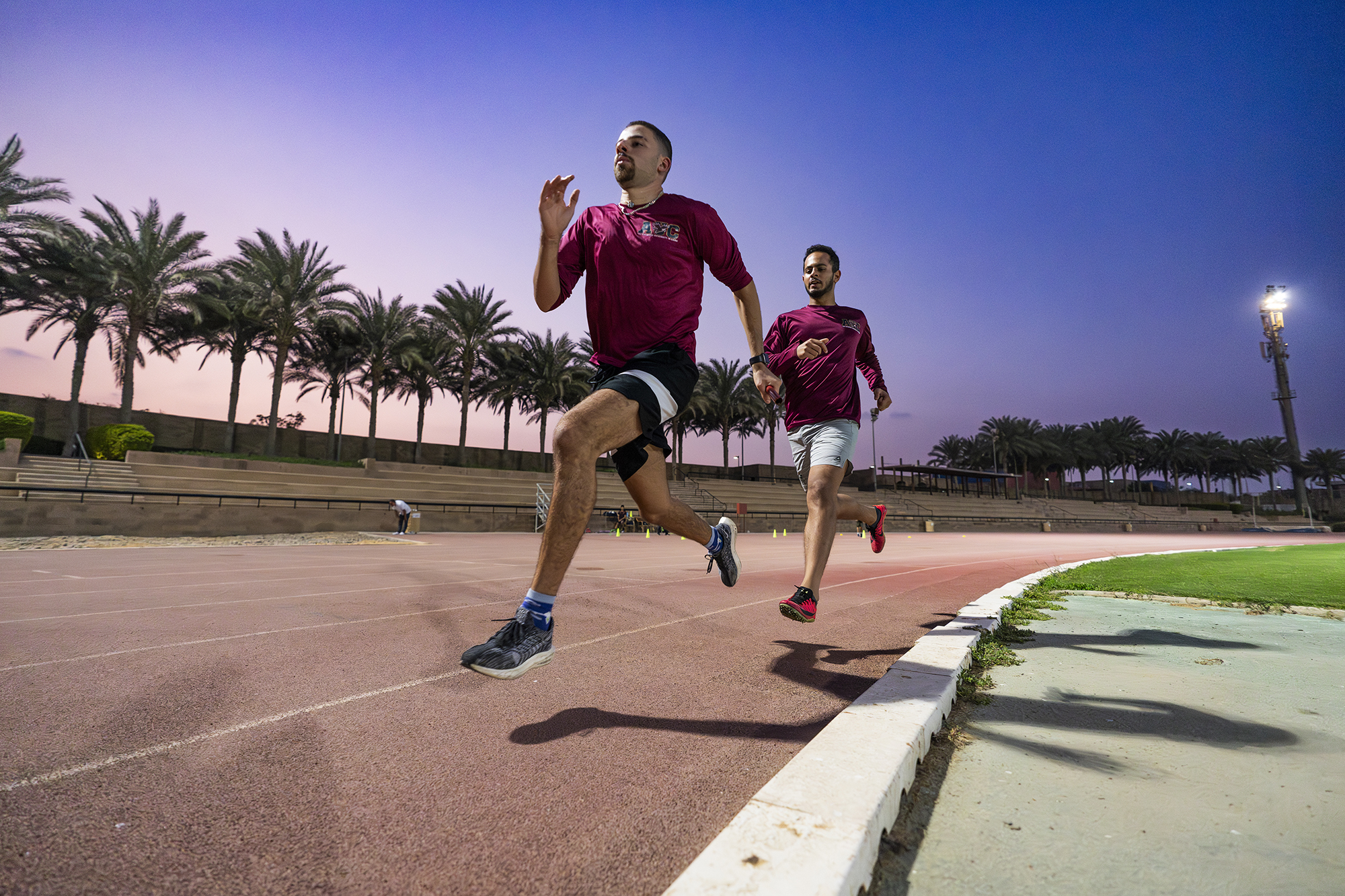 two male athletes running the track wearing maroon tshirts