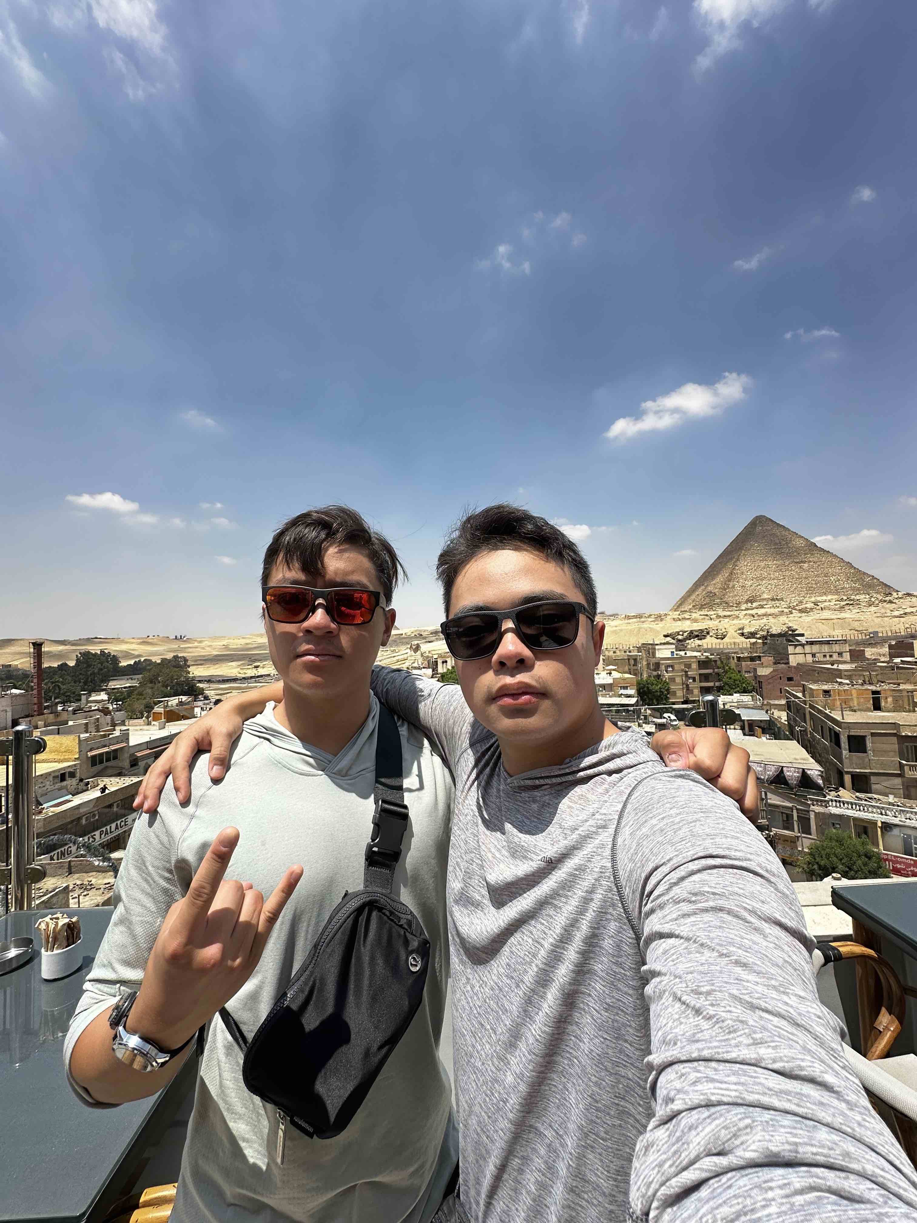 two boys wearing sunglasses taking a selfie and smiling at the camera