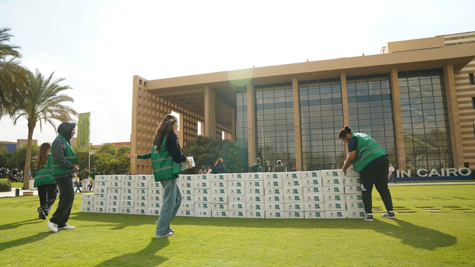 three girls packing boxes of goods infront of the AUC Library building