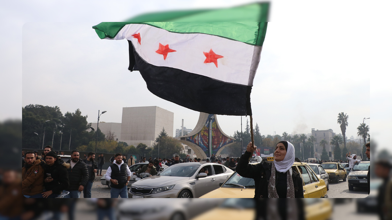 A woman waving the opposition flag with cars around her in a street in Syria