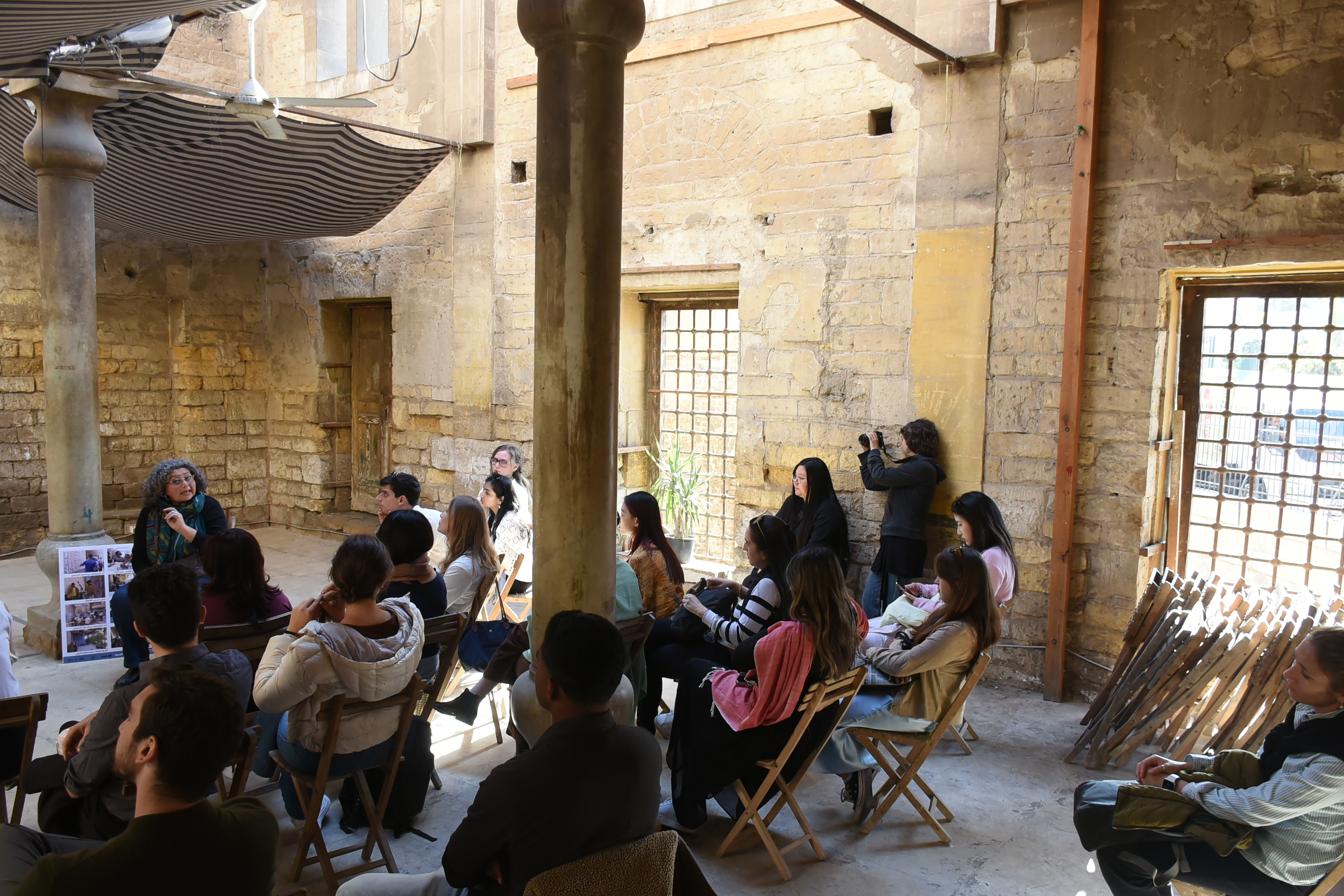 Students sit and listen to an AUC faculty in a historical site