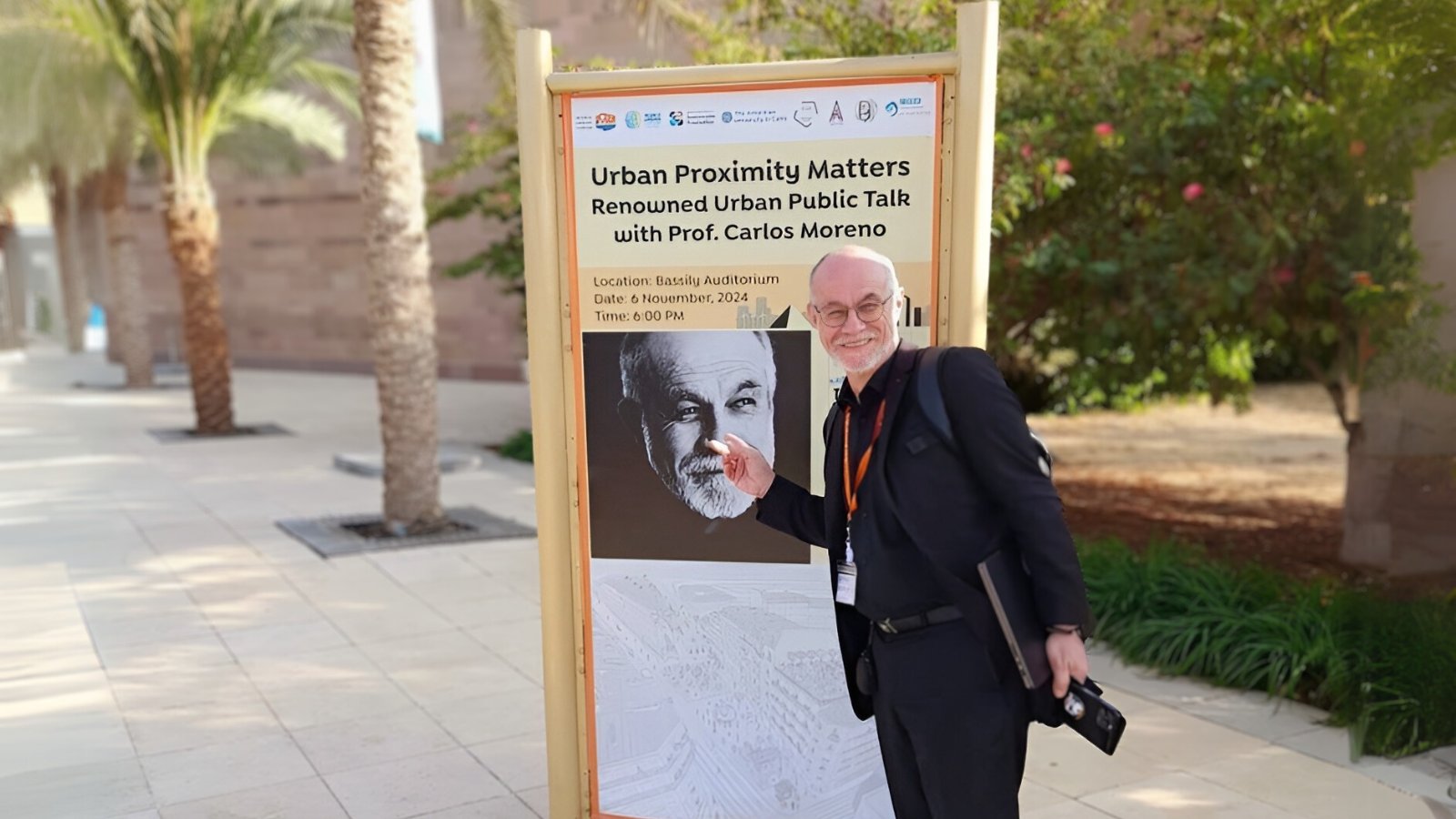 Carlos Moreno smiles and points at a poster with his picture, advertising his talk on AUC's campus.