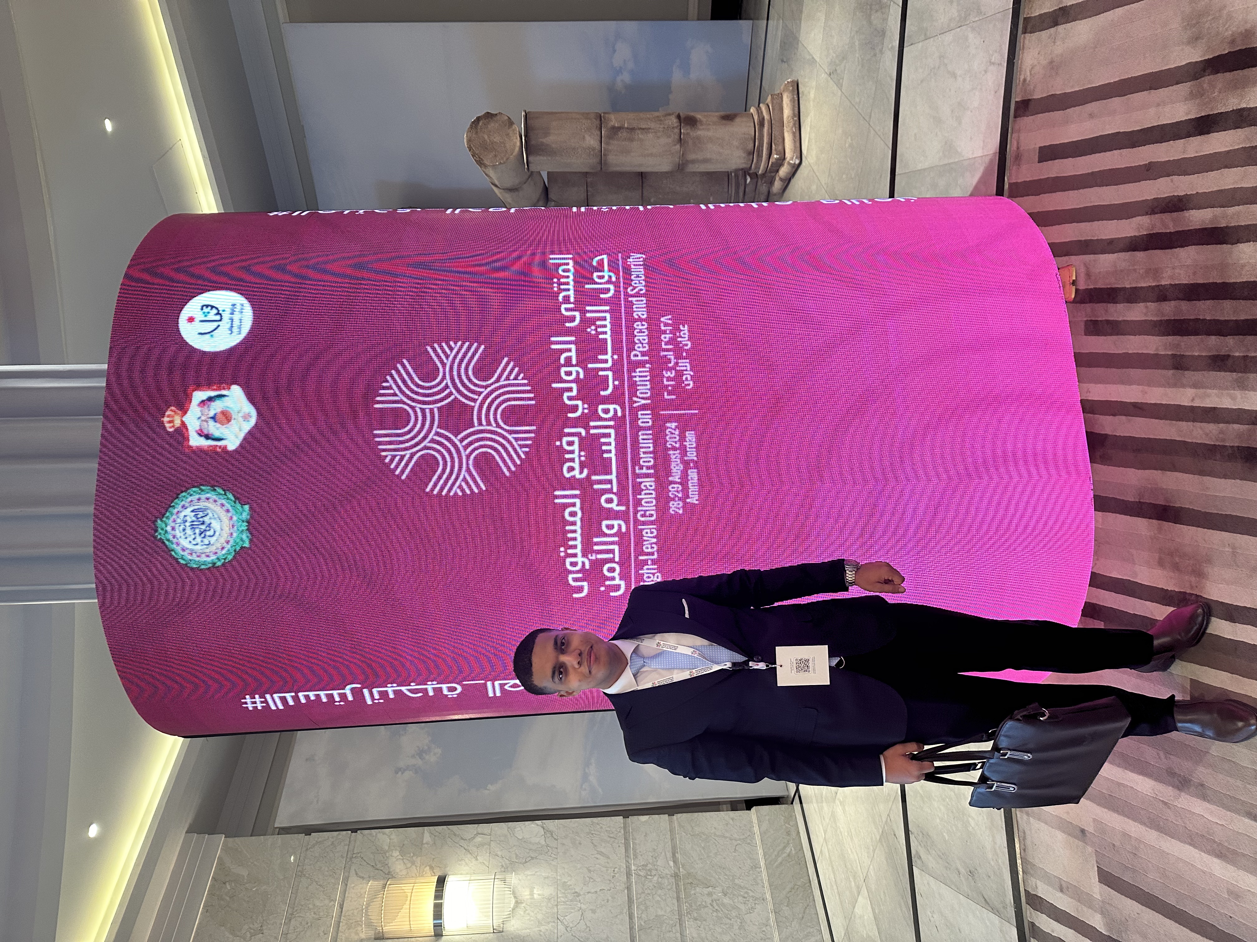 Man in suit holding briefcase stands in front of a sign for the Youth Forum