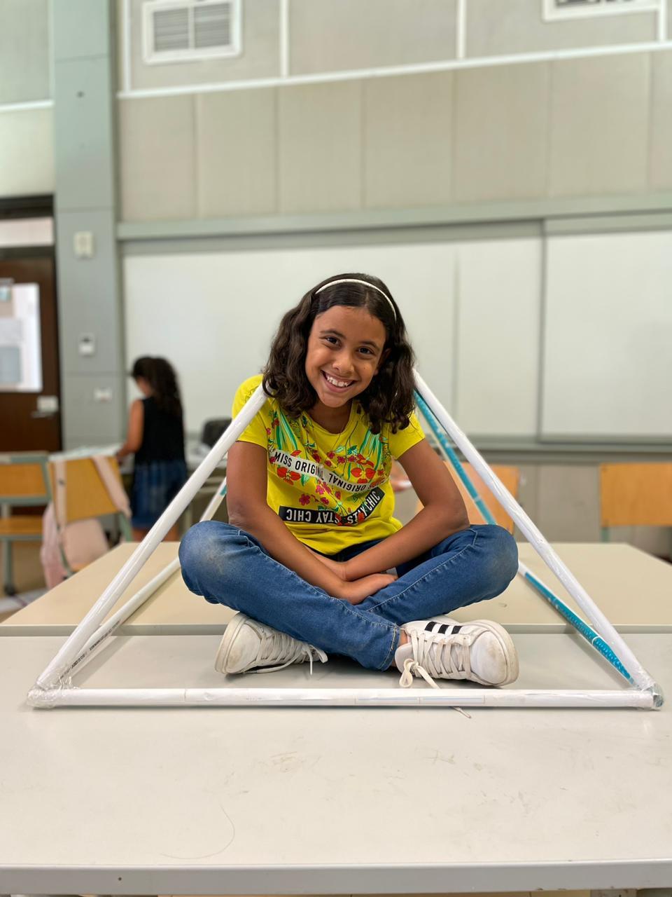 A young student sitting on a desk with a pyramid wrapped around her made out of resourceful materials