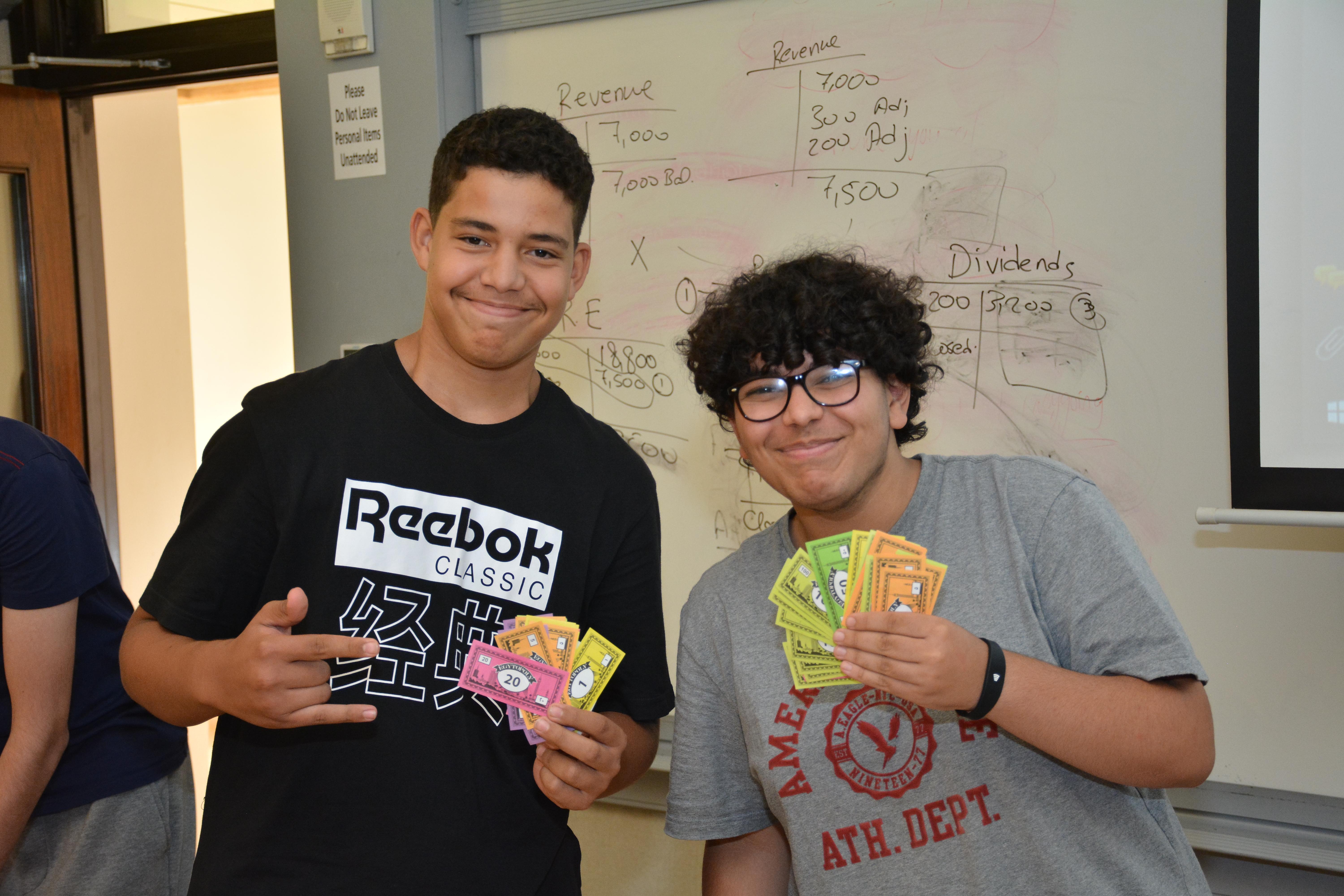 2 students in class holding monopoly cards