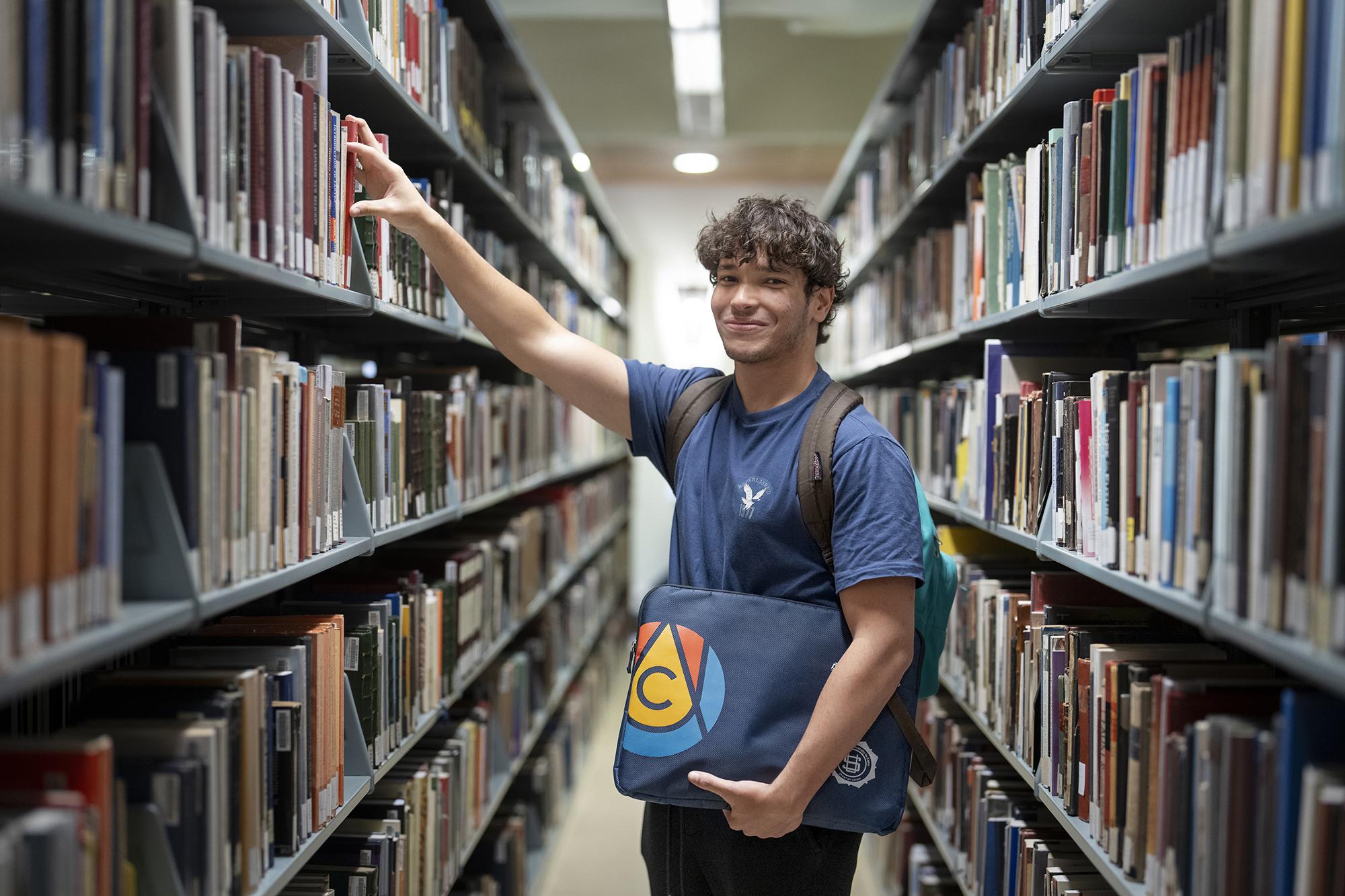 A male student is standing in a library in front of book shelves
