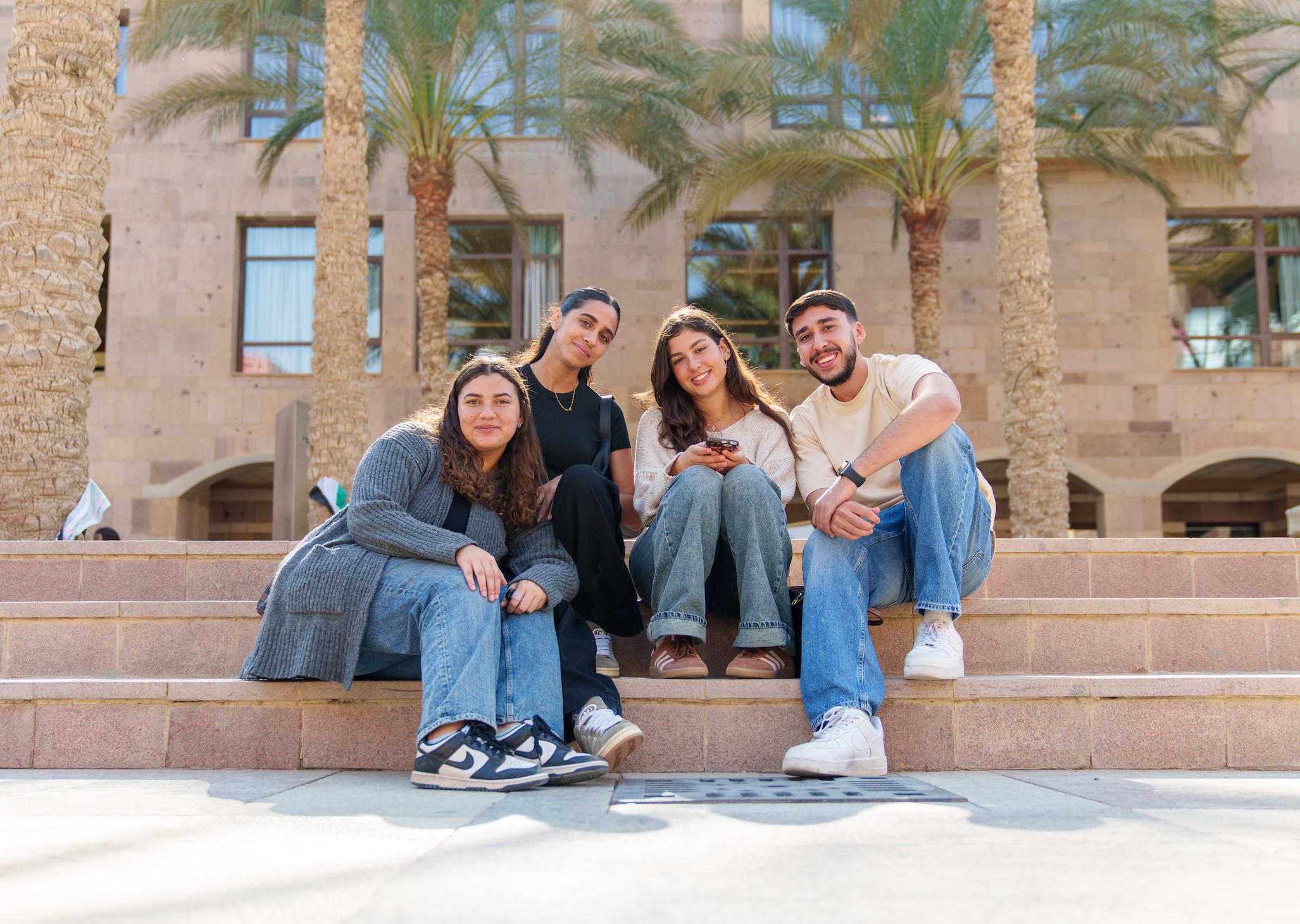 a group of girls and boys sitting together on the stairs on campus