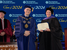 A professor in a cap and a gown holds a certificate next to the President of AUC.