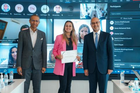 two men wearing a suit and a women wearing a pink jacket standing in the middle holding a certificate