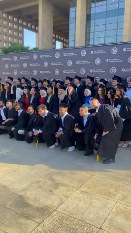 A group of students standing to get their picture taken. They are wearing their caps and gowns. Text: The American University in Cairo