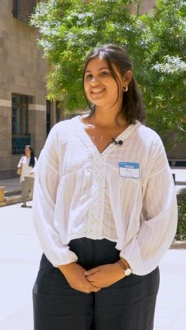 A female is standing and smiling. She is holding her hands together