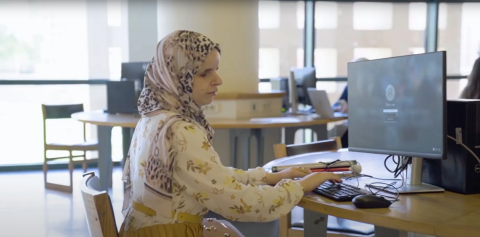 A veiled female student, Sohaila Fathy, is sitting and writing on a keyboard in front of a computer screen indoors