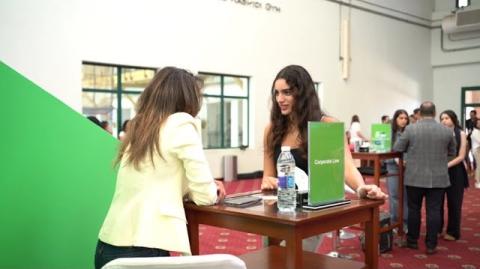 Two females are talking together over a table in a gathering of people