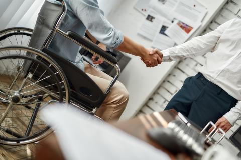 Man in wheelchair shakes hand with man standing up.