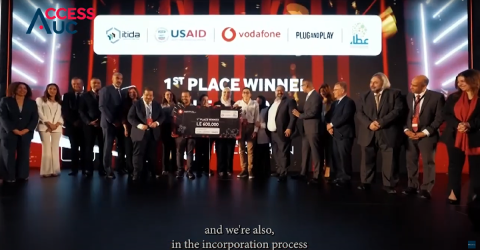 People standing to celebrate. The winner is standing in the middle holding a cheque. Text: AccessAUC. Itida. USAID.Vodafone. Plug and Play. عطاء. LE 600,000. 1st Place Winner