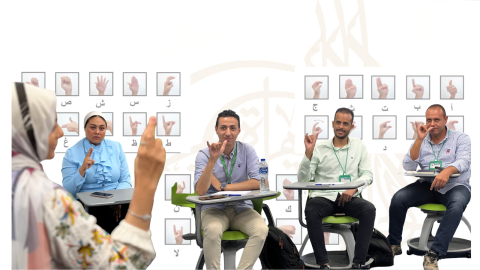 Images of participants in the workshop signing Egyptian Sign Language while watching the instructor, overlayed on a presentation background of the Arabic alphabet in sign language