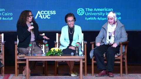 Three women sitting next to each other in separate chairs. One of them is talking into a microphone