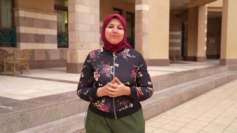 A veiled female is talking. She is wearing a flowery jacket and green pants