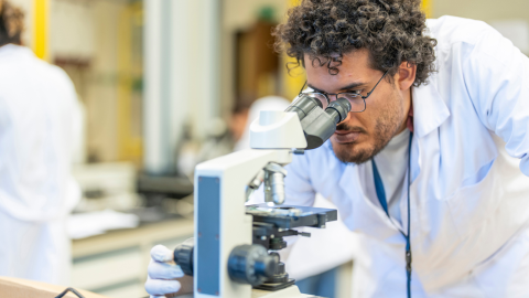 A male student wearing a lab coat and looking into a microscope in a lab at AUC