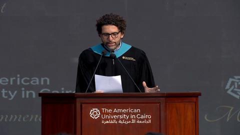 A male is talking at a podium, He is wearing a graduation gown. Text: The American University in Cairo