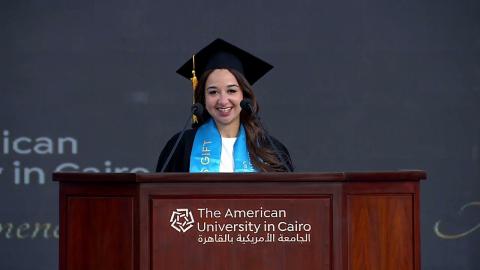 A female is talking at a podium, She is wearing a graduation gown. Text: The American University in Cairo