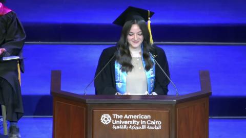 A female is talking at a podium, She is wearing a graduation gown. Text: The American University in Cairo