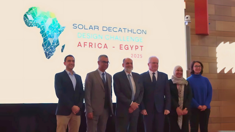 Administrators stand in front of a stage with a projection that reads "Solar Decathlon Design Challenge Africa - Egypt" with a play button