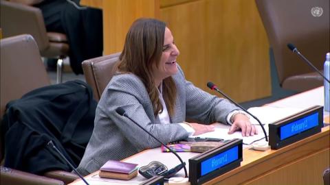 A woman is sitting at a panel, there is a microphone in front of her. She is smiling