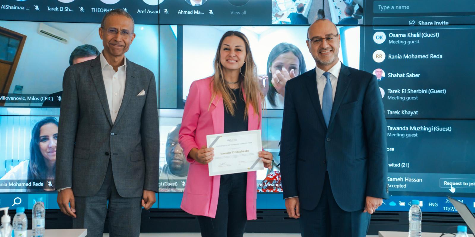 two men wearing a suit and a women wearing a pink jacket standing in the middle holding a certificate