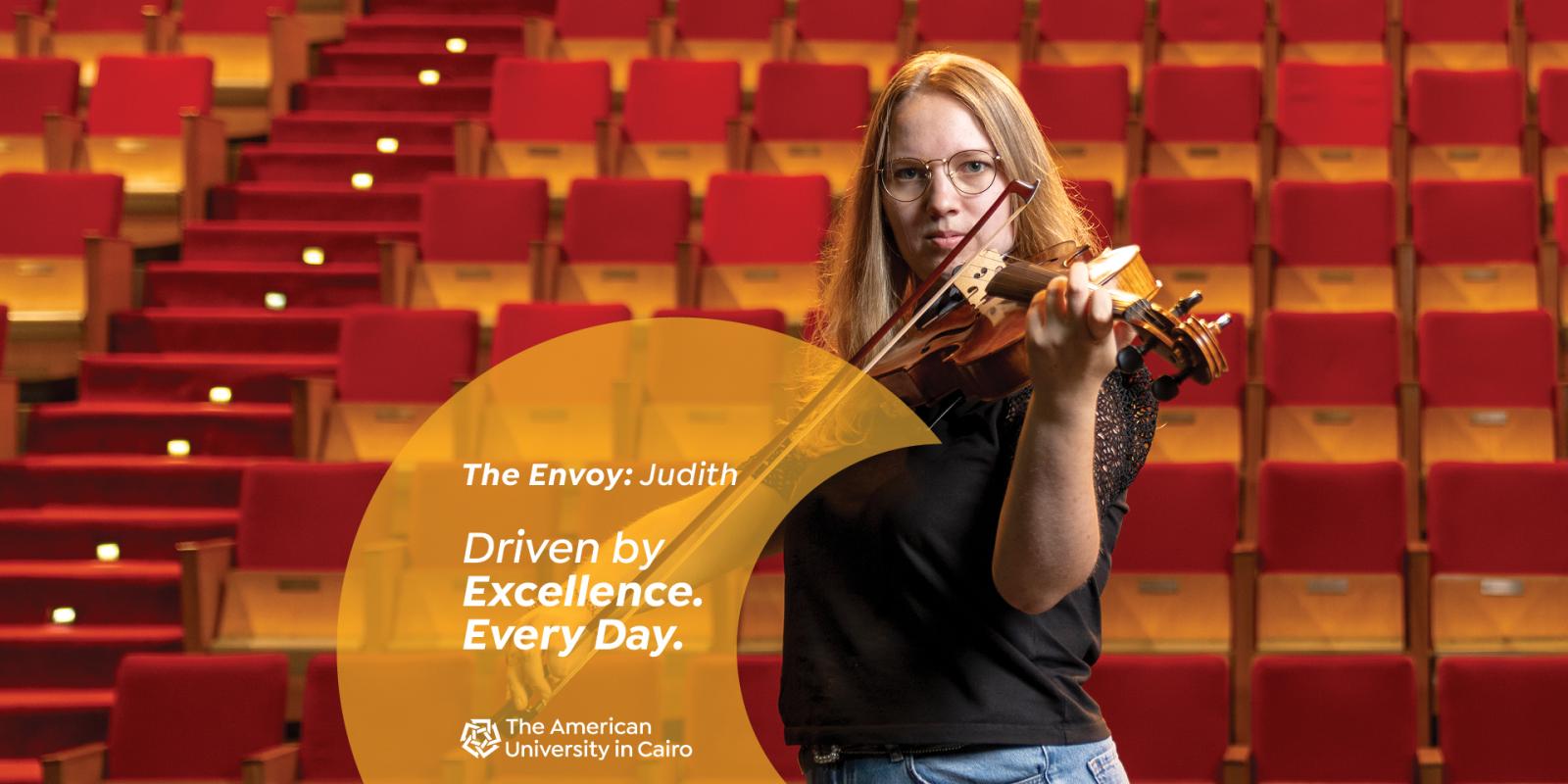 A female wearing glasses playing the violin in front of stage seats. Text reads "The Envoy: Judith. Driven by Excellence. Every Day. The American University in Cairo"