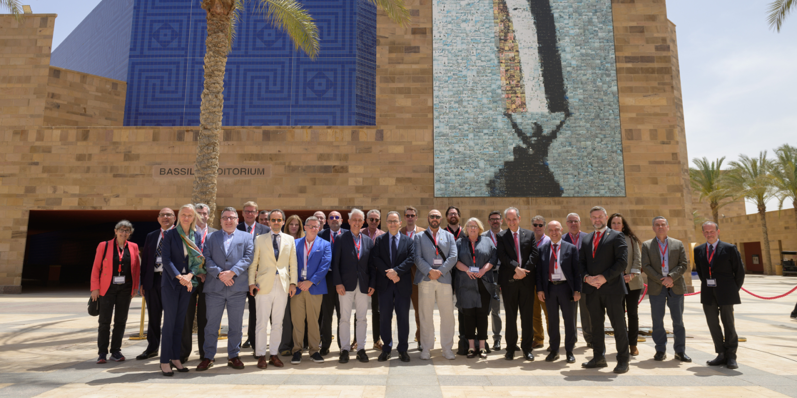 Many people in business casual wear pose in front of a tall beige building