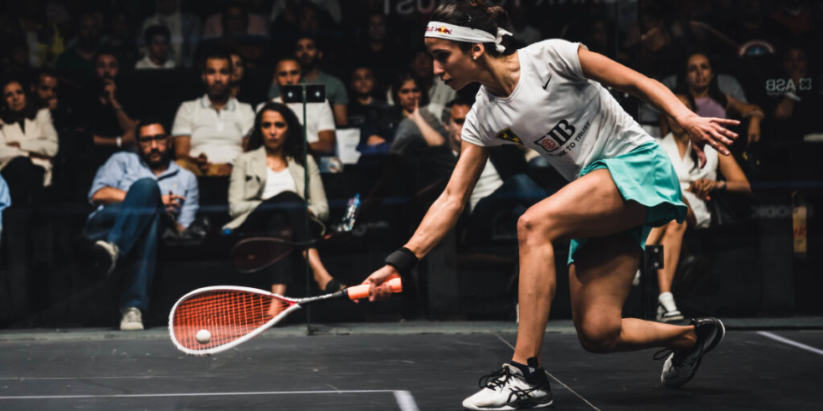 A woman is playing squash in front of an audience