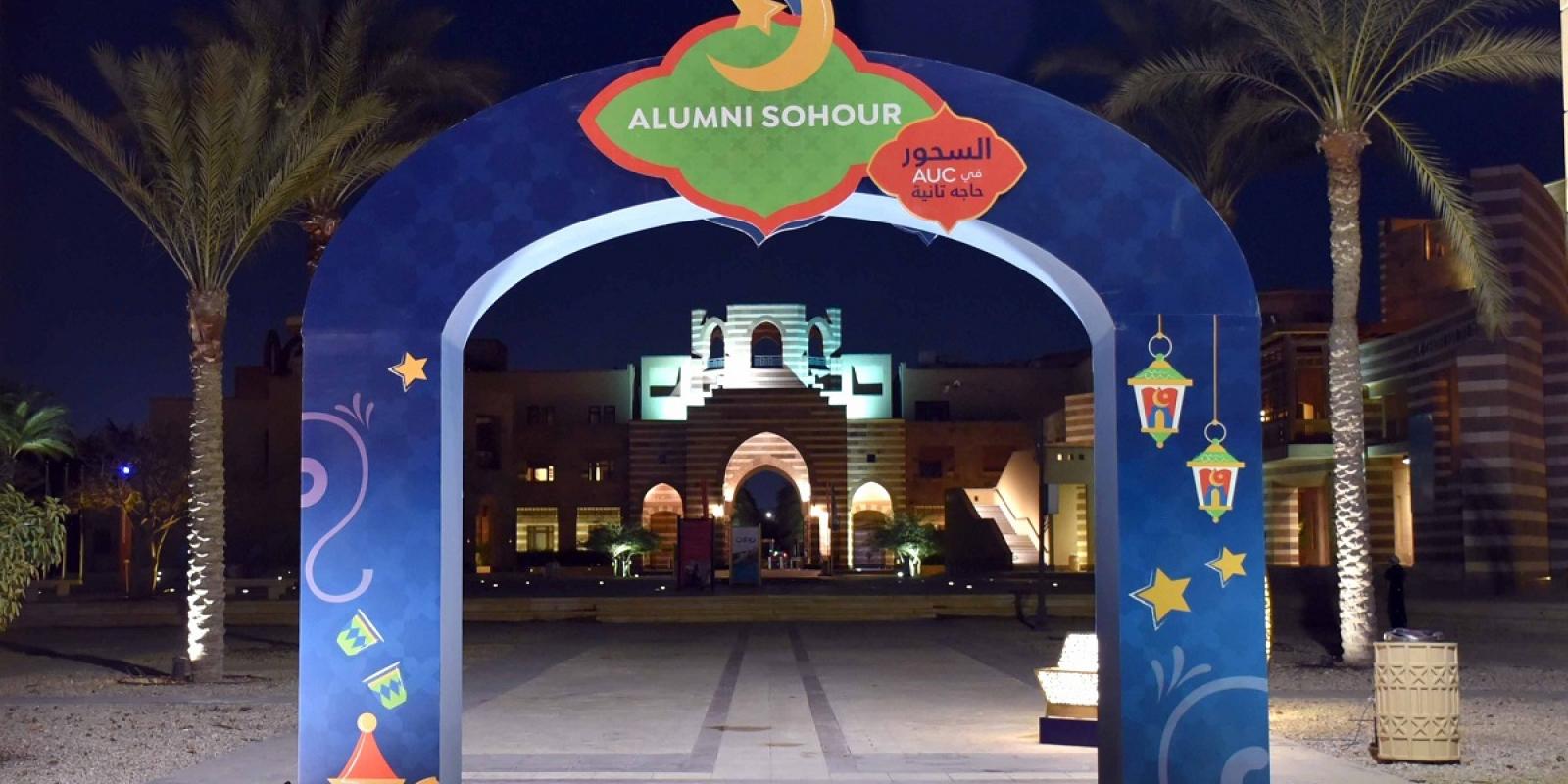 An arch that has drawings of lanterns, stars and a crescent. Text: Alumni Sohour. السحور فيِAUC حاجة تانية