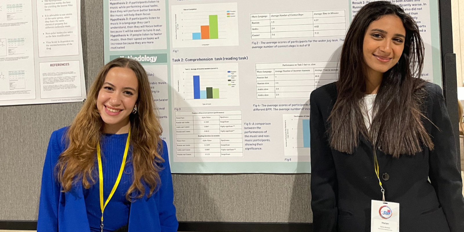 Two women, one in a blue jacket and another in a black jacket, smile in from of a large scientific poster