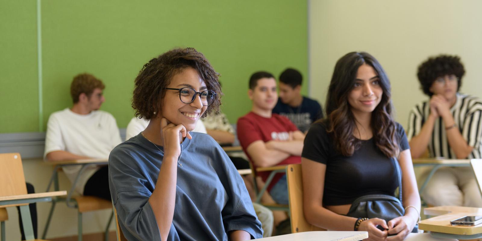 A girl with short hair sitting in a classroom smiling