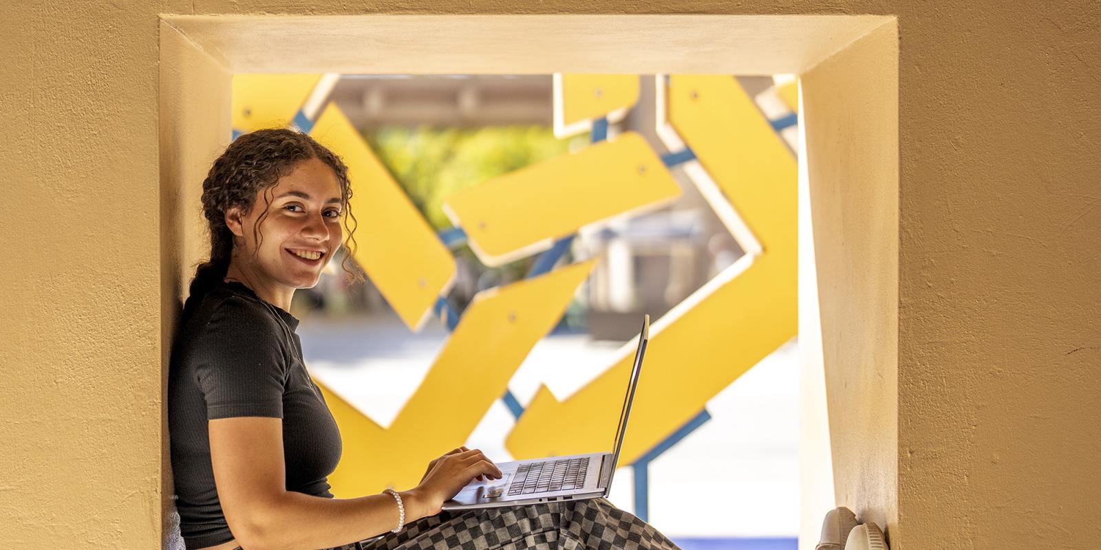 A girl sitting in a cube smiling at the camera with AUC star behind her