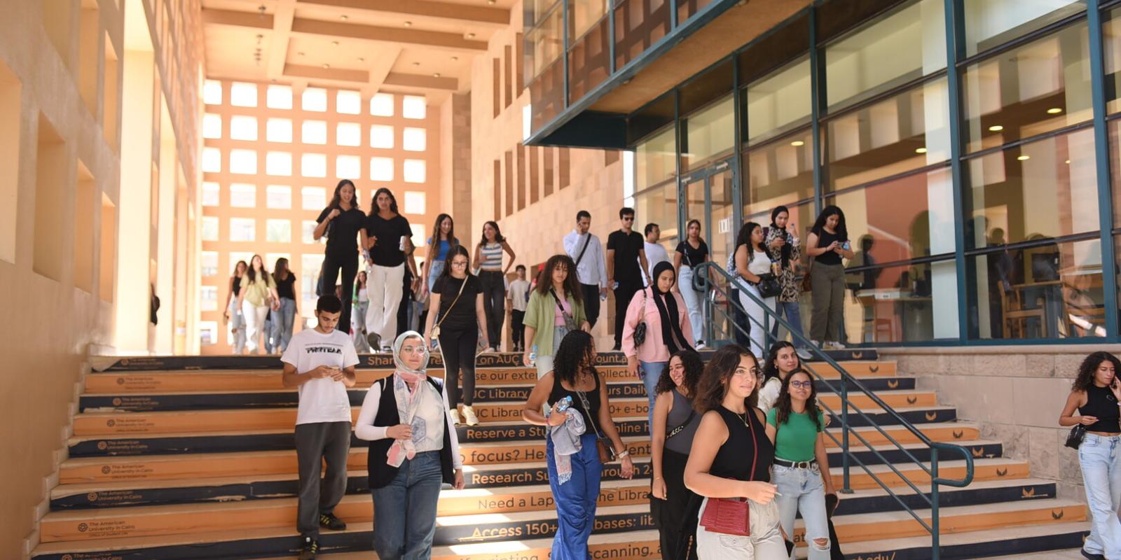 a group of students going down the stairs in front of the AUC Library building