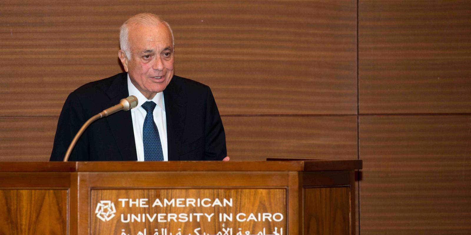 AUC Advisory Trustee Nabil Elaraby standing in front of an AUC podium speaking through a microphone