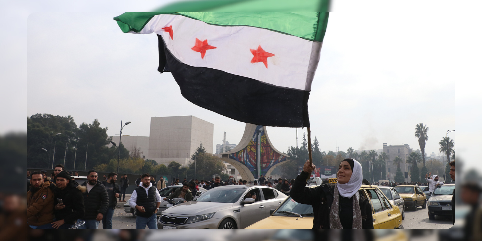 A woman waving the opposition flag with cars around her in a street in Syria