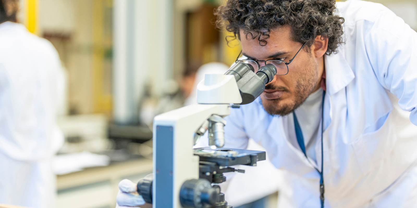 A male student wearing a lab coat and looking into a microscope in a lab at AUC