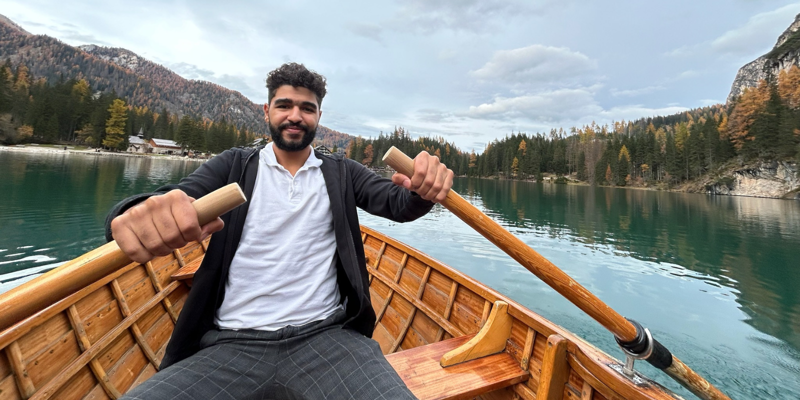 Ahmed Ayman sits in a row boat in beautiful Italian lake scenery