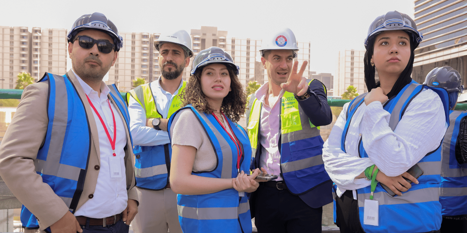 Five people, including students, in construction vests and helmets looking off into the distance