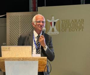 man in suit stands behind a podium holding a microphone