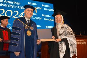Woman in cap and gown stands next to the AUC President holding a certificate