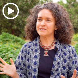 a woman with curly brown hair wearing a dotted bouse with a black shirt underneath