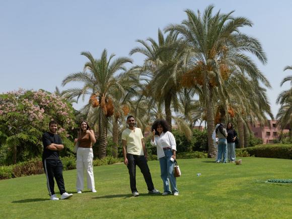 Males and females are standing on greenery surrounded by palm trees and trees